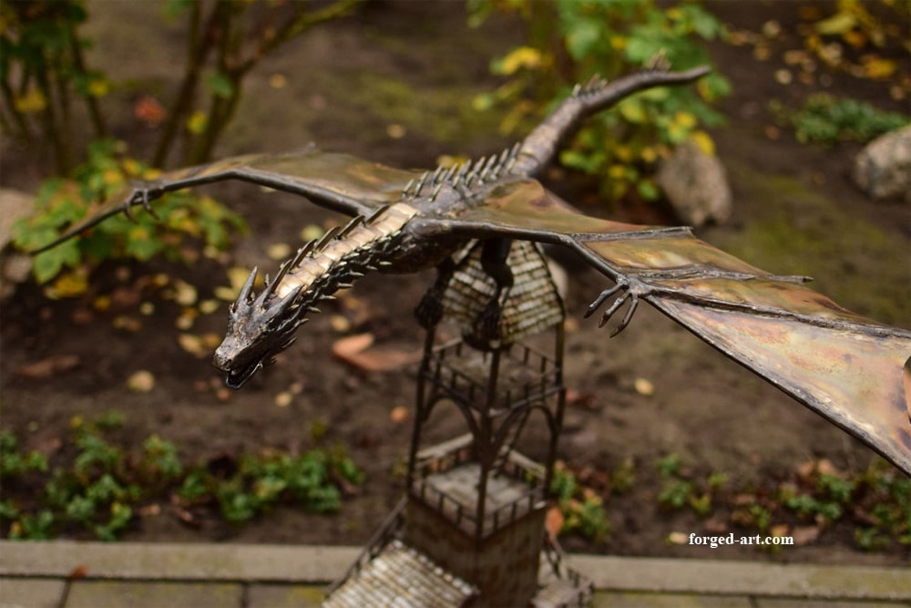 Forged dragon sculpture spreading its wings over a tower
